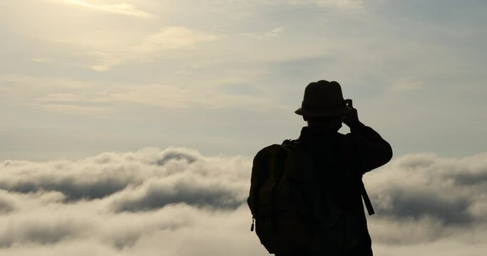 The silhouette of backpackers taking pictures on mountain peak above clouds, tourists with beautiful moving clouds.
