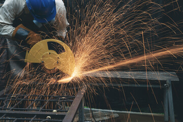 Man wearing helmet, mask and glove using electric steel cutter machine working at workshop. Male cutting steel with sparks flying. Hard work factory or garage industry in construction site concept.