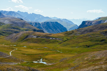 Great rocky mountains and deep gorge behind beautiful green valley with lake in highlands. Awesome mountain landscape with giant rockies and deep abyss. Wonderful scenery with big rocks and precipice.