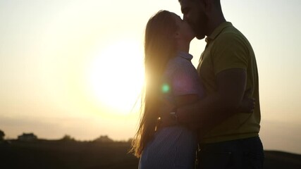 Silhouette of man and woman at sunset. Beautiful girl kisses guy in a deserted field, leaves and rises to hold her hands in slow motion. A romantic date and love on nature of loving happy couple