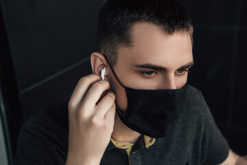 Handsome brunette male listening to music using white wireless headphones. Young european businessman or entrepreneur with gadgets in roadside cafe. Corona virus pandemic, covid19. Quarantine concept.