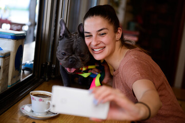 Young girl enjoying her free time with her adorable Blue French Bulldog and taking selfies inside a small, cosy, rustic pet friendly cafe.
