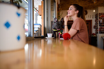 Beautiful girl enjoing her free time, while drinking coffee with her Blue French Bulldog in a cozy pet friendly cafe