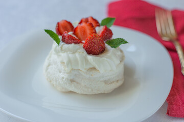 Closeup Pavlova meringue cake with whipped cream, fresh strawberry and mint on white plate. Australian cuisine.