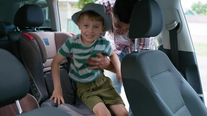 safe ride, loving father puts his little cute male child in back seat in baby car seat and fasten safety belts during a joint trip with kid in ca