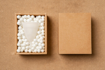 Fototapeta na wymiar Menstrual cup eco friendly reusable and silicone in in a craft box in white balls isolated on beige background