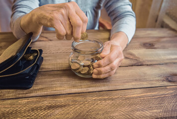 Old wrinkled hand holding jar with coins, empty wallet, wooden background. Elderly woman throws a coin into a jar, counting. Saving money for future, retirement fund, pension, poorness, need concept.