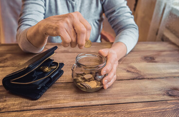 Fototapeta na wymiar Old wrinkled hand holding jar with coins, empty wallet, wooden background. Elderly woman throws a coin into a jar, counting. Saving money for future, retirement fund, pension, poorness, need concept.