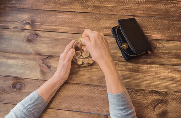 Old wrinkled hand holding jar with coins, empty wallet, wooden background. Elderly woman throws a coin into a jar, counting. Saving money for future, retirement fund, pension, poorness, need concept.