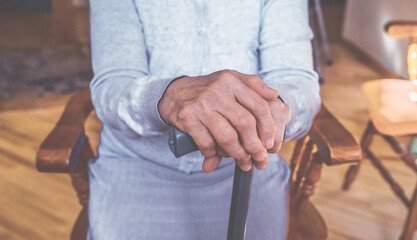 Old wrinkled hands on walking stick. Hands of a sitting senior woman holding a cane. Pension, care, poorness, need concept.