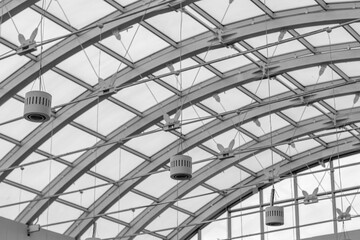 Fototapeta na wymiar The transparent roof of a large shopping center in the form of an arch with lamps. Black and white photographs of buildings.