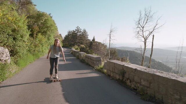 Smiling dreadlocks woman longboarding on mountain and sea background riding skateboard on road on sunny day enjoying summer vacation, Montenegro. Slow motion
