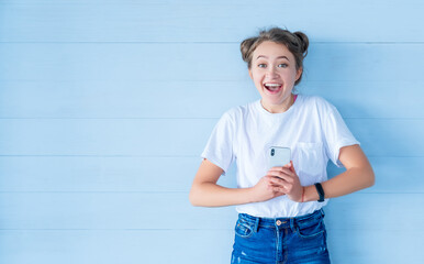 Female with smartphone in casual clothes on blue wooden backdrop. Surprised expression. Empty space. Modern lifestyle.