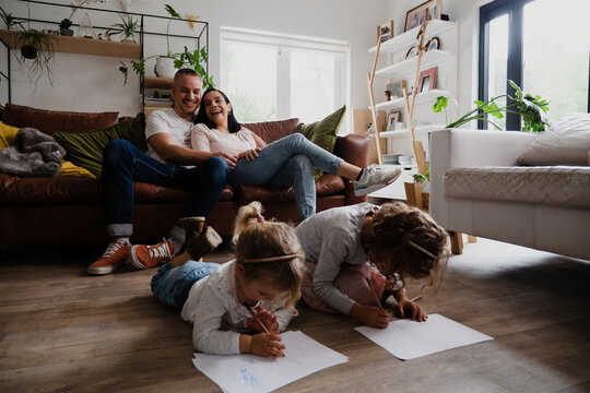 Caucasian family in the living room together, spending quality family time. Kids drawing on the floor while mother and father laugh together