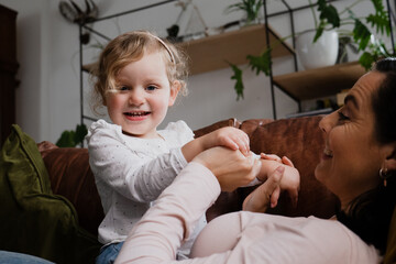 Mother and young baby daughter playing on the sofa, having fun together at home