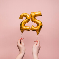 Female hand holding a number 25 birthday anniversary celebration gold balloon