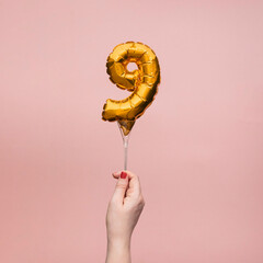 Female hand holding a number 9 birthday anniversary celebration gold balloon