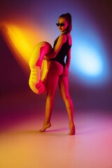 Seductive young girl' portrait on bicolored neon studio background in neon. Fit sportive woman in bodysuit with rubber donut. Facial expression, summer, weekend, beauty, resort concept. Vacations.