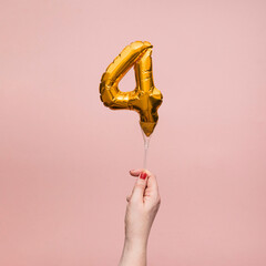 Female hand holding a number 4 birthday anniversary celebration gold balloon © ink drop