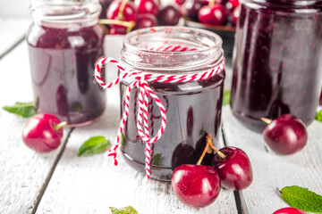 Jar of cherry jam. Homemade sweet and sour cherry jam with fresh cherries on wooden white table, copy space