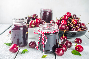 Jar of cherry jam. Homemade sweet and sour cherry jam with fresh cherries on wooden white table, copy space