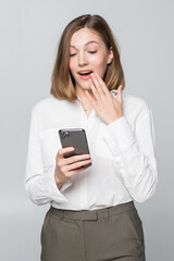 Young businesswoman with shocked face expression is using smartphone on white background