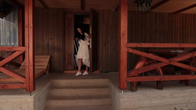 Rear view of a beautiful slim young brunette woman with suitcase leaves hotel room after long therapeutic vacation. Female goes on business trip leaving house, luggage, tourism, departure, fees travel