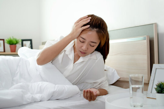 Asian woman is taking a headache medication on the bed. She has a headache and can't work.