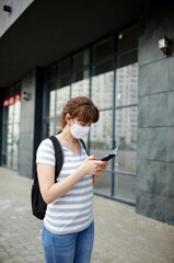 Woman during COVID-19 and flu outbreak with face protection mask. Holding mobile phone at street during quarantine.Concept of coronavirus quarantine. Air pollution