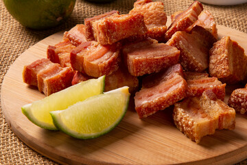 Deep fried crispy pork belly served with two half lemon on the table.