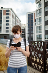 Woman during COVID-19 and flu outbreak with face protection mask. Holding mobile phone at street during quarantine.Concept of coronavirus quarantine. Air pollution