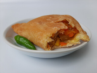 Bitten pastel. Pastel is a popular snack from Indonesia. A pastry filled with chicken meat and mixed vegetable, then deep fried. Served with green chili. On white plate. Isolated in white background.