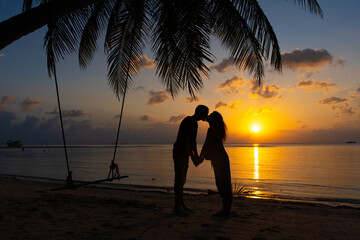 Silhouetted couple in love kisses on the beach during sunset.