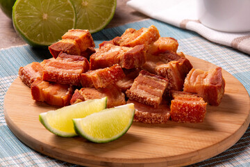 Deep fried crispy pork belly served with two half lemon on the table.