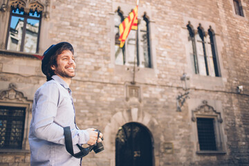 Adult stylish photographer with digital camera laughing while standing at entrance of medieval building