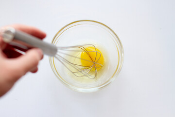 Whisking fresh eggs in glass bowl on white table. Whipped eggs.