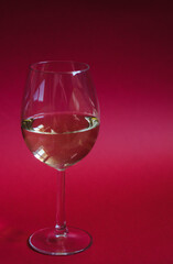 Glass of white wine on a red background. Vertical photo