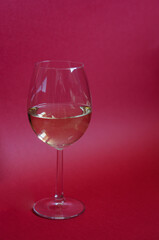 Glass of white wine on a red background. Vertical photo