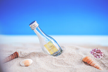 bottle on sand beach with seashell over blurred tropical blue sea and clear blue sky