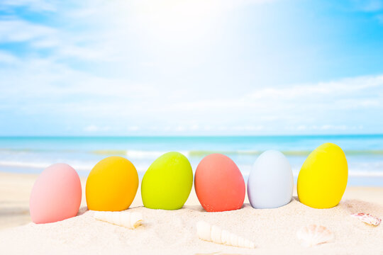 colorful eggs on white sand beach over blue background,happy Easter or summer holiday concept.