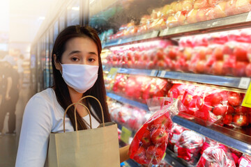 Asian woman wearing protective face mask hold paper shopping bag in supermarket department store. Girl, looking grocery to buy  some fruit. New normal after covid-19. Family concept.