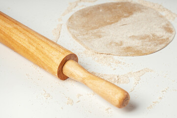 The dough is rolled out in a circle on a white table near the rolling pin