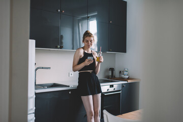 Cheerful blond woman using phone at kitchen