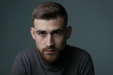 Portrait of a young bearded guy of twenty-five years old, looking at the camera, close-up. Studio photo on a gray background.