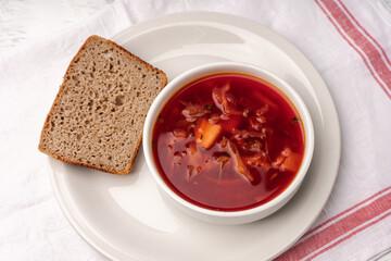Borscht in a white tureen next to a piece of wholemeal bread top view