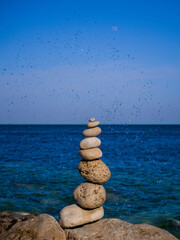 stack of stones on the beach, wave crashing behind