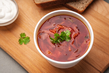 Borscht decorated with greens in a disposable dish next to sour cream and bread top view
