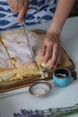 Woman cutting homemade traditional Greek pastry -- Bougatsa made with phyllo dough and semolina custard cream into pieces.
