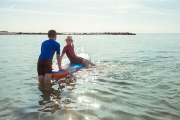 Obraz premium Two happy siblings teen children in neoprene suits having fun with sup board in Baltic sea