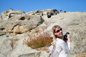 Georgia, Tbilisi - October 21, 2019: Attractive beautiful young girl who is female photographer traveller holding modern mirror camera in the hands outdoors in the mountains